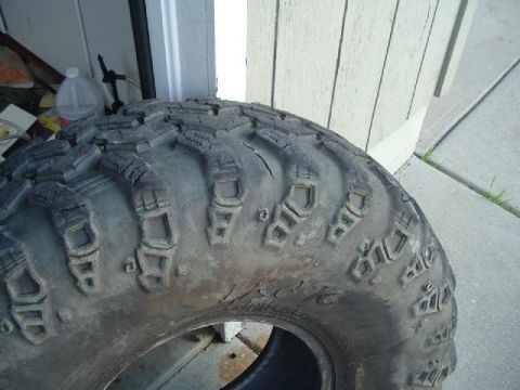 1989 Ford Bronco - A close-up view of a single, heavily used off-road tire, showing its tread pattern and some sidewall markings.