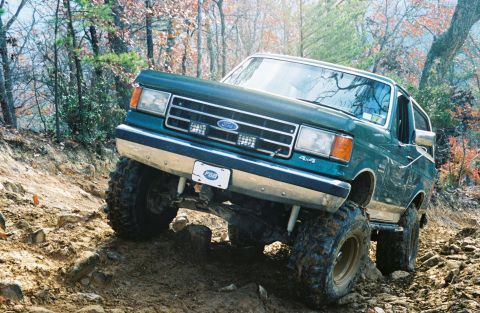 1990 Ford Bronco - 1990 Ford Bronco navigating a challenging off-road trail with steep inclines and loose rocks.