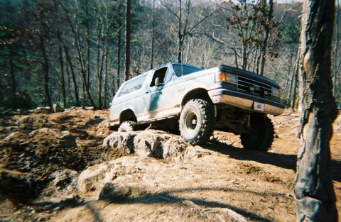 1990 Ford Bronco - This 1990 Ford Bronco navigates a challenging rocky trail in a wooded area.