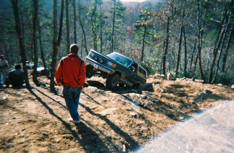 1990 Ford Bronco - A dark-colored Ford Bronco navigates a steep, rocky incline in a wooded area.