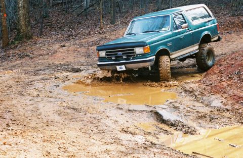 1990 Ford Bronco - This 1990 Ford Bronco navigates a challenging muddy terrain in a wooded area.