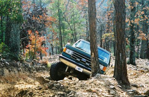 1990 Ford Bronco - 1990 Ford Bronco navigating a challenging off-road course through a wooded area.