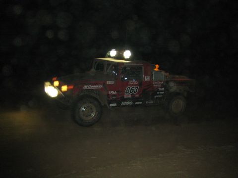 1990 Ford Bronco - red boxy Hummer-style off-road race vehicle numbered 863 with BFGoodrich decals drives at night with lights on.