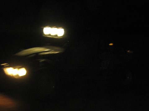1990 Ford Bronco - off-road vehicle with a glowing roof light bar and headlights drives through near-total darkness, captured with motion blur.