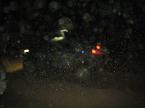 1990 Ford Bronco - very dark, blurred nighttime photo showing the faint outline of a vehicle with red tail lights amid lens spots.