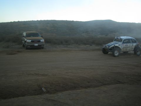 GMC SUV and white off-road buggy parked on dirt at dusk