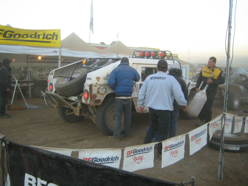 Crew around white off-road vehicle at BFGoodrich pit at dawn