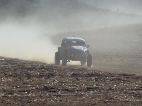 Silver off-road race buggy charging through thick dust on a barren desert course