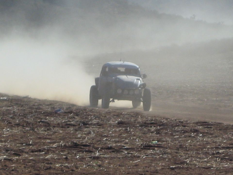 Silver off-road race buggy charging through thick dust on a barren desert course