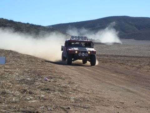 Dark red Hummer-style off-road racer speeding on dirt course raising dust