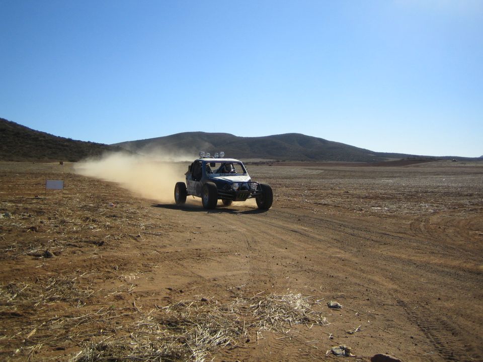 Single-seat off-road buggy racing across open desert flat trailing dust