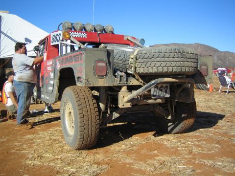 Rear view of red Hummer race truck numbered 863 with spare tire, person working on it