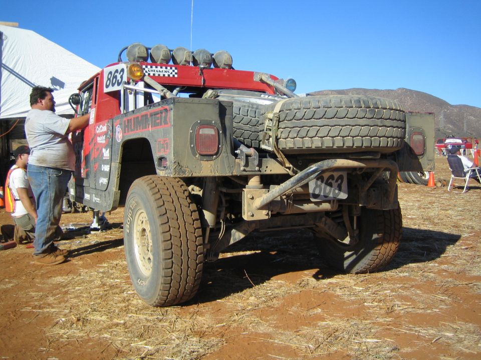 Rear view of red Hummer race truck numbered 863 with spare tire, person working on it