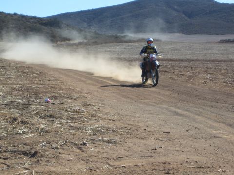 Helmeted rider on dirt motorcycle riding down dusty desert trail