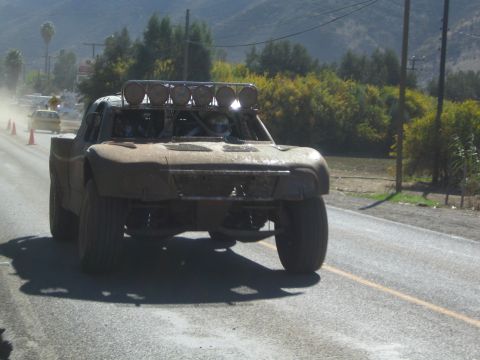Mud-caked off-road trophy truck driving head-on down a paved highway