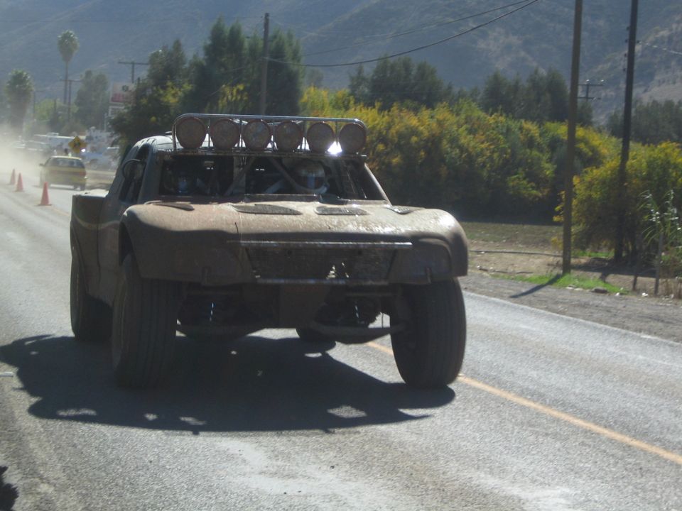 Mud-caked off-road trophy truck driving head-on down a paved highway