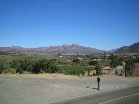 Scenic valley view of green fields and mountains beyond a roadside shoulder