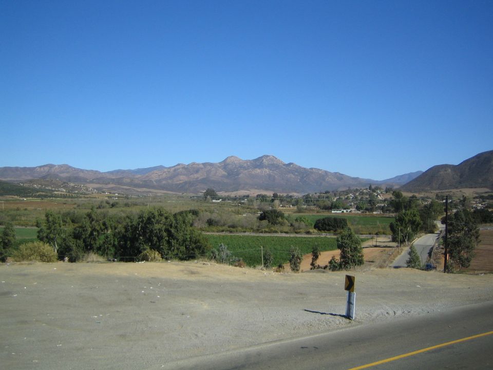 Scenic valley view of green fields and mountains beyond a roadside shoulder