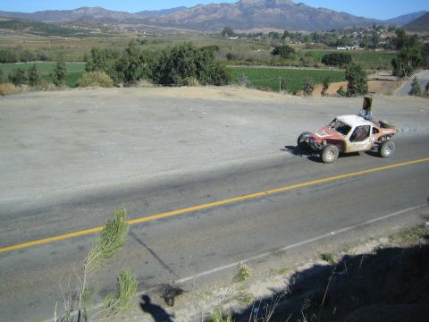 Off-road race buggy with white roof speeding along a paved rural road