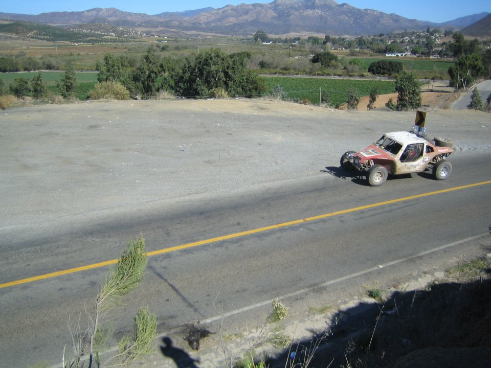 Off-road race buggy with white roof speeding along a paved rural road