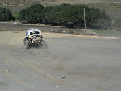 White Baja Bug race car kicking up dust on a dirt track marked 572