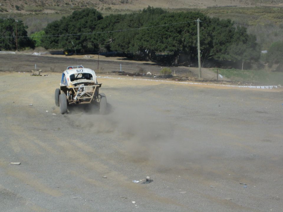 White Baja Bug race car kicking up dust on a dirt track marked 572