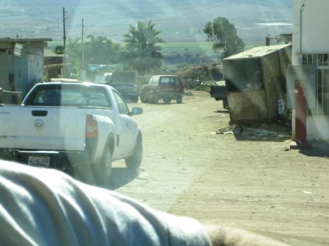 White pickup truck on a dusty dirt road through a roadside settlement
