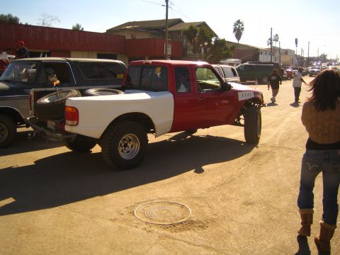 Lifted red and white prerunner pickup parked on a dirt street