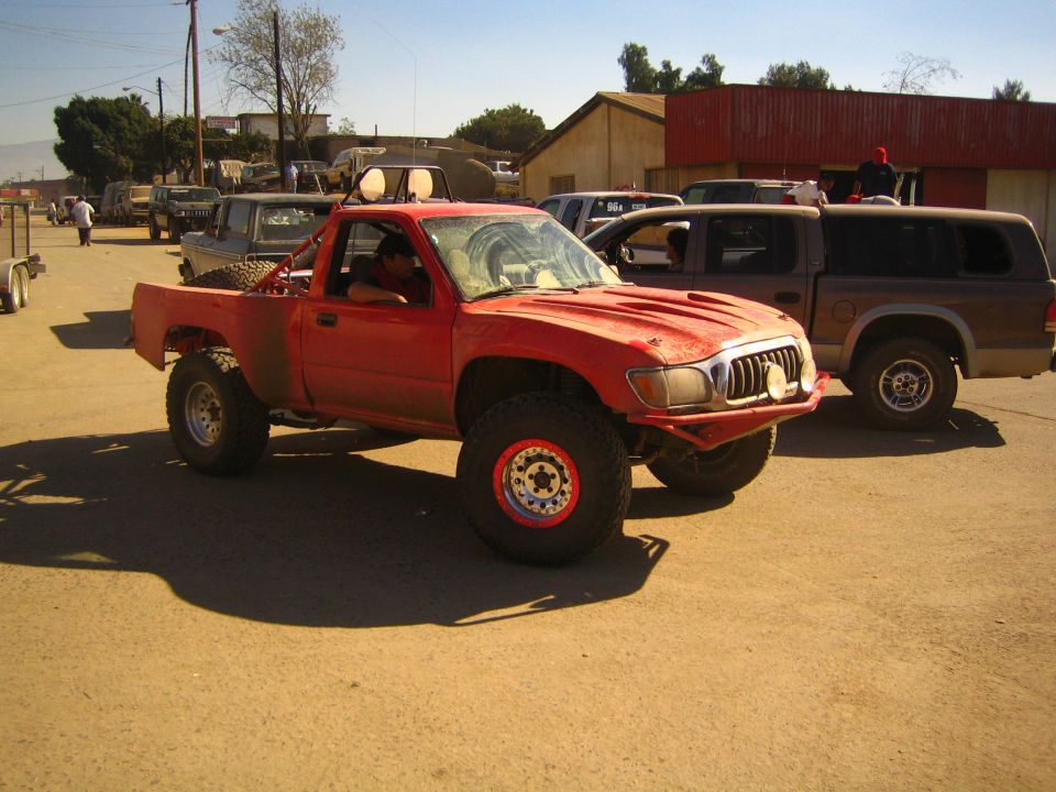 Lifted red prerunner pickup with fender flares parked in a dirt lot