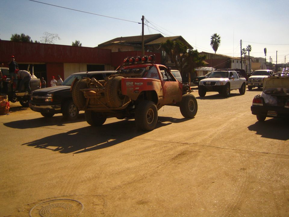 Trophy-style off-road race truck driving down a dusty town street