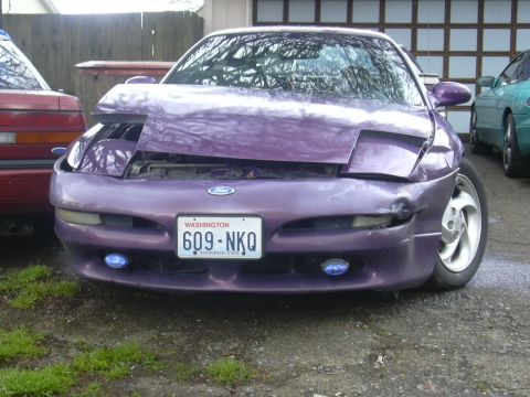 1997 Ford Probe - Front view of a purple Ford Probe with crumpled passenger-side front damage and missing trim; Washington plate reads 609-NKQ.