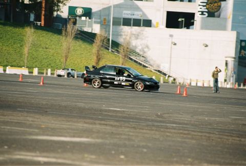 1997 Ford Probe - A black Mitsubishi Lancer Evolution navigates a course marked by orange cones, with another vehicle in the distance.