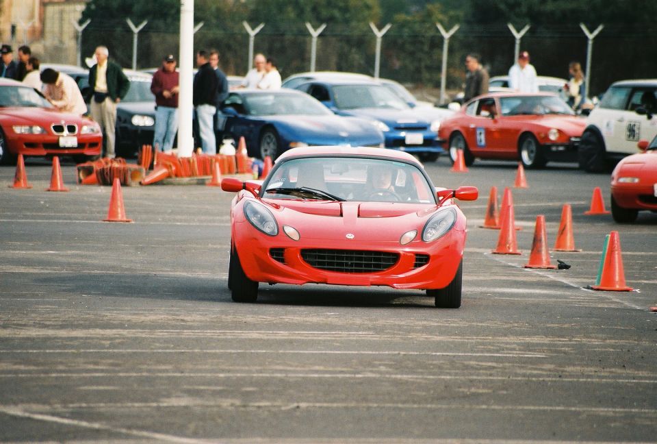 Front view of a red Lotus Elise driving on a track with orange cones
