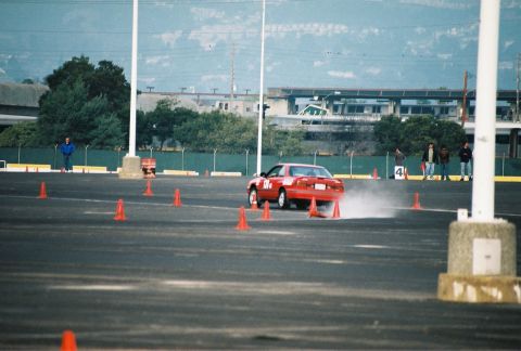 1997 Ford Probe - A red coupe performs a drift maneuver on a cone-marked asphalt course.