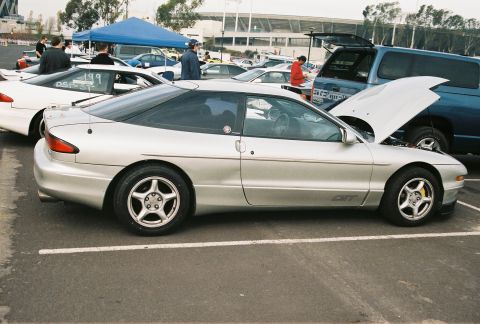 1997 Ford Probe - A silver Ford Probe is parked in a lot with other vehicles, including a white Probe and a blue SUV with its hood open.