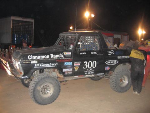 1990 Ford Bronco - Side view of a black Cinnamon Ranch off-road race truck numbered 300 in a night pit under floodlights.
