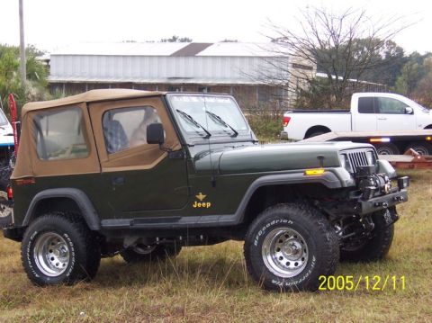 1989 Ford Bronco - A green Jeep Wrangler is parked on grass next to a white pickup truck on a trailer.