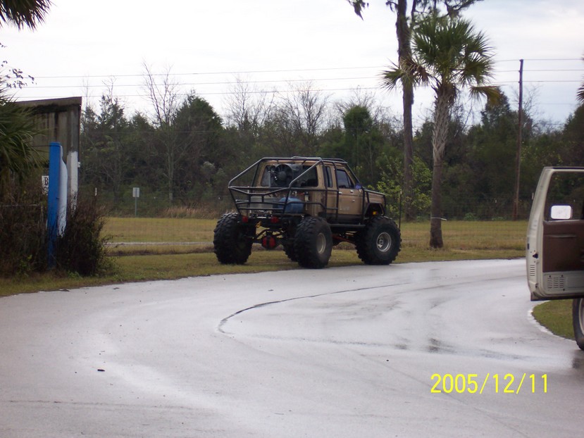 Tan off-road truck with roll cage and oversized tires parked on wet pavement