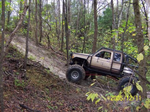1989 Ford Bronco - A heavily modified off-road truck navigates a steep, wooded trail, its off-road capabilities.