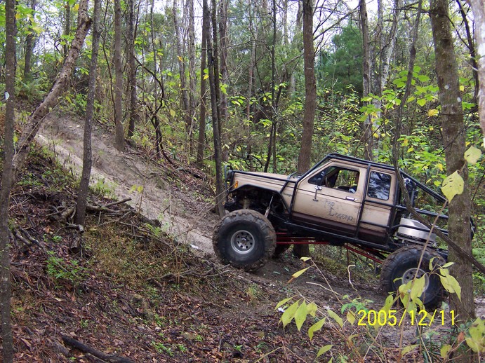Modified off-road truck with large tires climbing a dirt hill in a forest