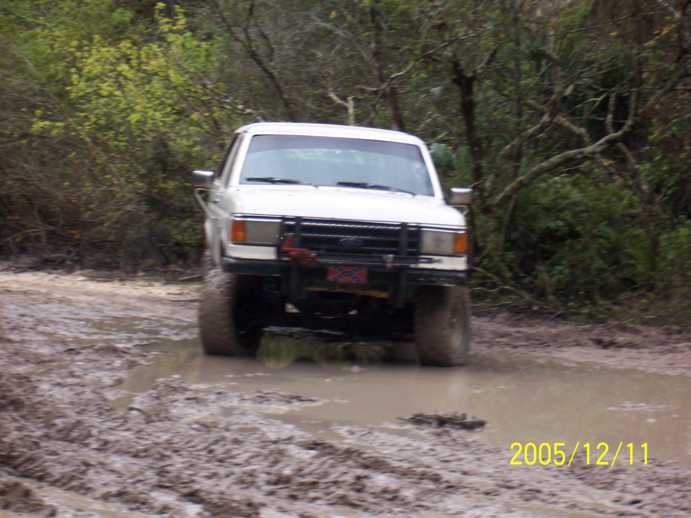 White 1989 Ford Bronco driving through mud