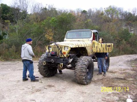 1989 Ford Bronco - Modified Jeep Wrangler with tiger stripe paint and large tires stands on a dirt path with two people.