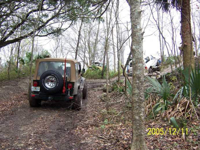 Brown Jeep Wrangler with spare tire on rear, on a muddy trail