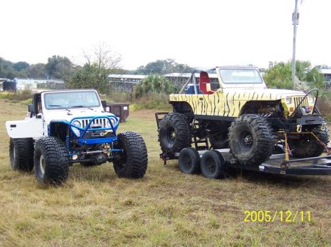 1989 Ford Bronco - Two heavily modified Jeeps, one white and one with tiger stripes, are parked outdoors on a grassy area.