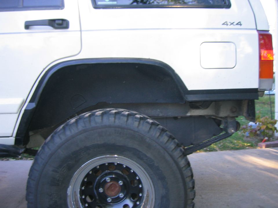 Rear quarter of white Jeep Cherokee with large mud tire and black steel wheel