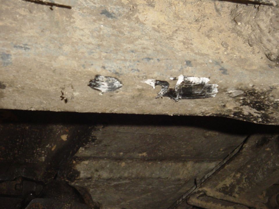 Undercarriage of a vehicle with white and black paint marks on a metal beam