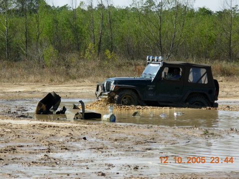 1987 Ford Bronco - A dark green Jeep Wrangler is stuck in a muddy puddle with debris in the foreground.