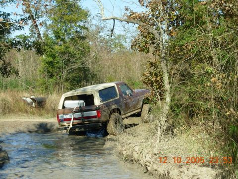 1987 Ford Bronco - This 1987 Ford Bronco navigates a muddy off-road trail, with its rear end submerged in water.