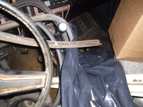 1981 Ford Bronco - The interior of a vehicle is cluttered with a steering wheel, trash bag, and a cardboard box.