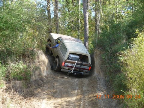 1987 Ford Bronco - A Ford Bronco navigates a steep, muddy off-road trail surrounded by trees.